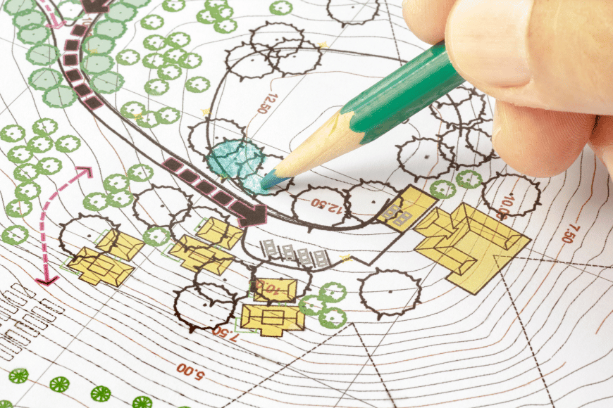 A hand holding a pencil over a detailed landscape architecture plan.