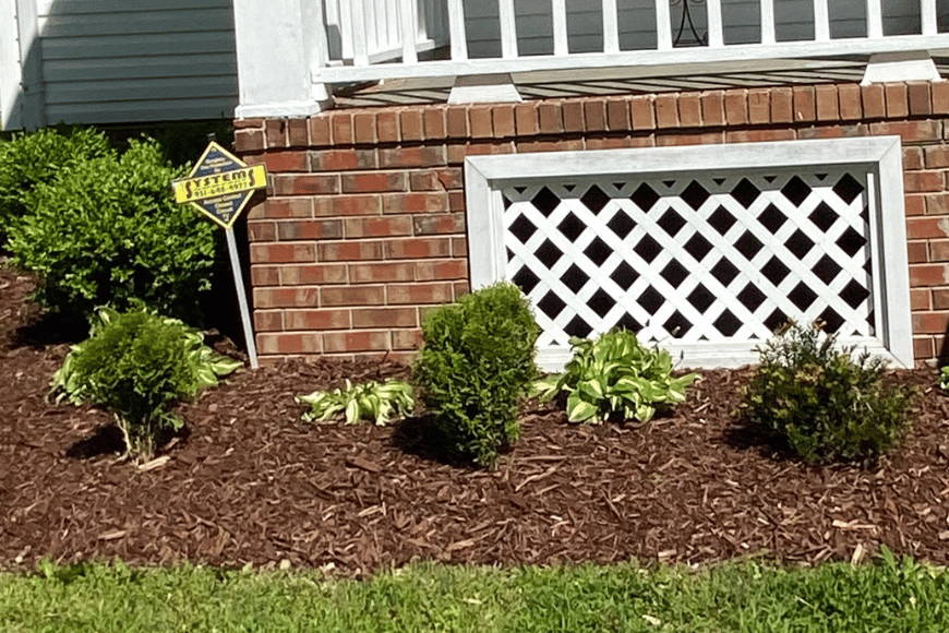 Well-manicured garden with mulch, shrubs, and a "beware of dog" sign in front of a house.