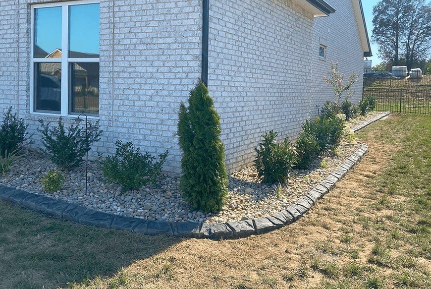 Landscaped house corner with shrubs and decorative stones.