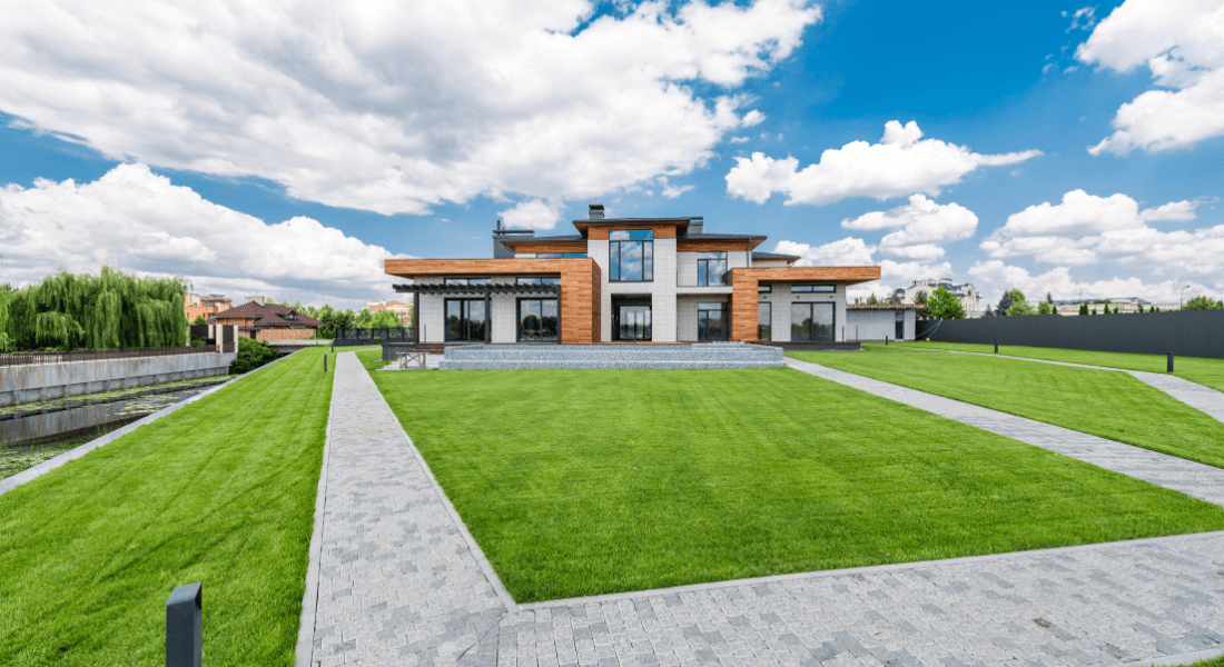 Modern house with large windows, wood accents, and manicured lawn under a partly cloudy sky, with stone pathways leading to the entrance. Landscape Clarksville TN